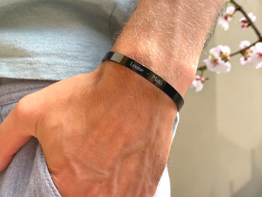Bracelet jonc homme noir gravé de prénoms porté au poignet, décor de fleurs de cerisier
