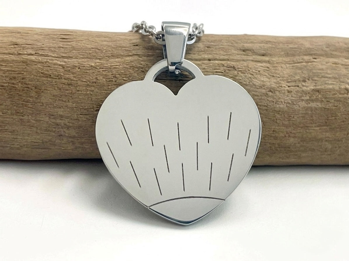 Collier cœur argenté gravé d'un motif soleil, posé sur une branche de bois clair
