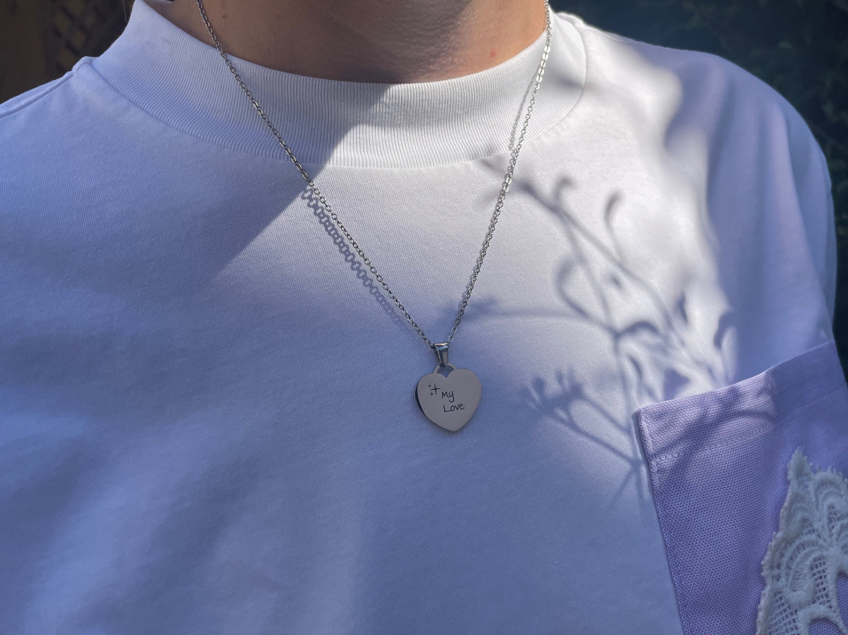 Collier cœur argenté porté au cou, sur un haut blanc