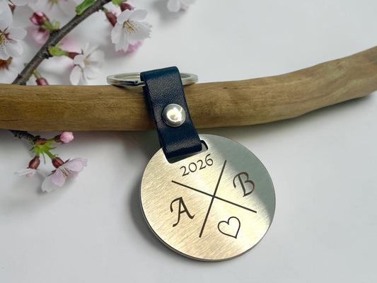 Porte-clés acier personnalisé avec initiales et année, posé sur une branche et des fleurs de cerisier
