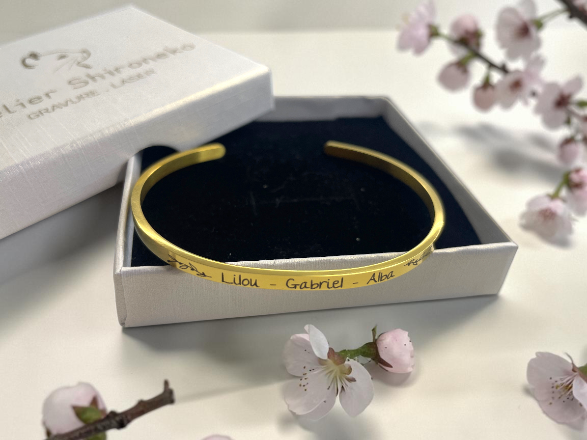 Bracelet jonc doré gravé de prénoms dans son écrin noir et blanc, décor de fleurs de cerisier