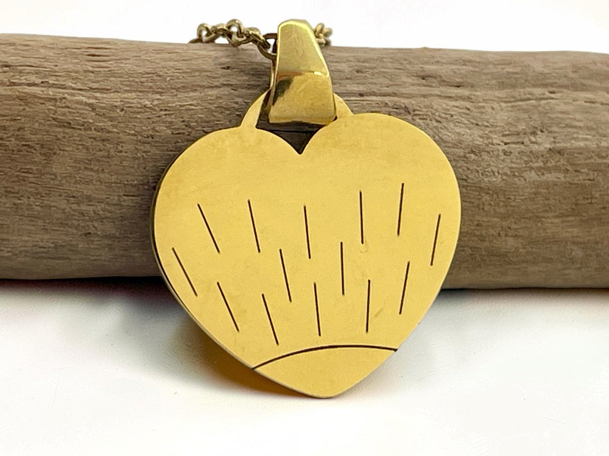 Collier cœur doré gravé d'un soleil rayonnant, suspendu à une branche de bois