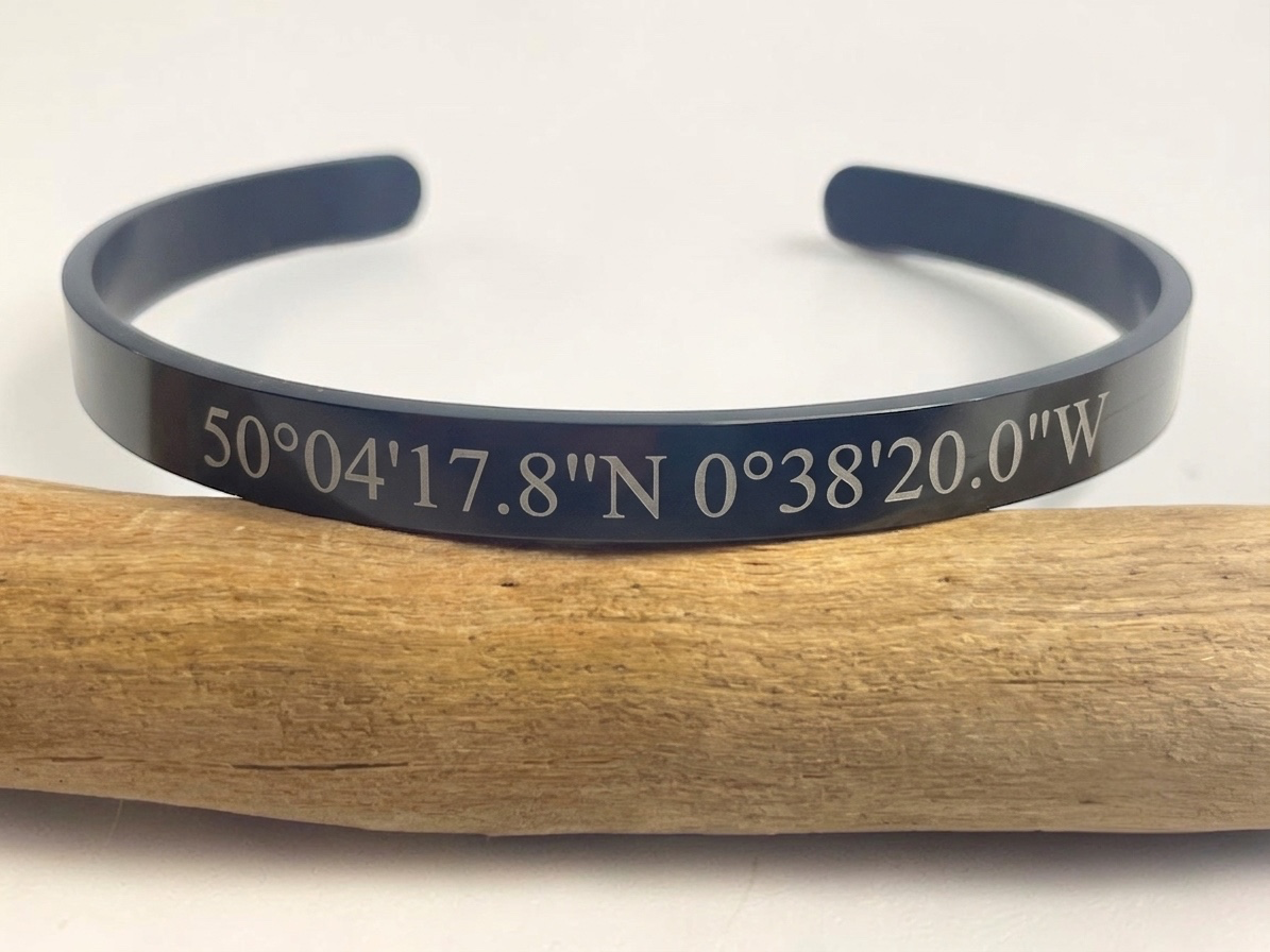 Bracelet jonc noir gravé de coordonnées GPS personnalisées, posé sur une branche de bois
