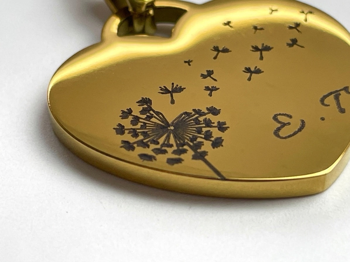 Gros plan de la gravure pissenlit et des initiales sur un collier cœur en acier doré