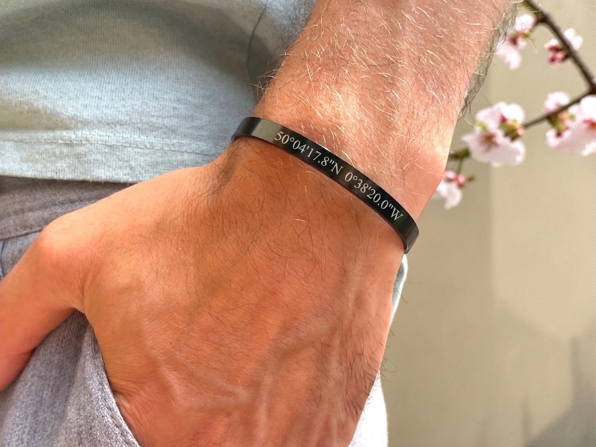 Bracelet jonc noir coordonnées GPS porté au poignet, décor de fleurs de cerisier
