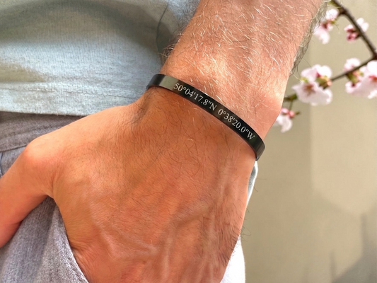 Bracelet jonc noir coordonnées GPS porté au poignet, décor de fleurs de cerisier