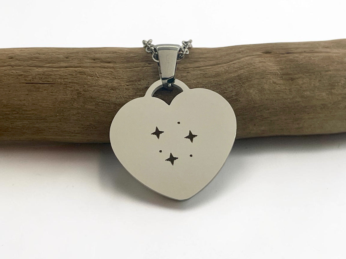 Collier cœur argenté gravé de petites étoiles, posé sur une branche de bois