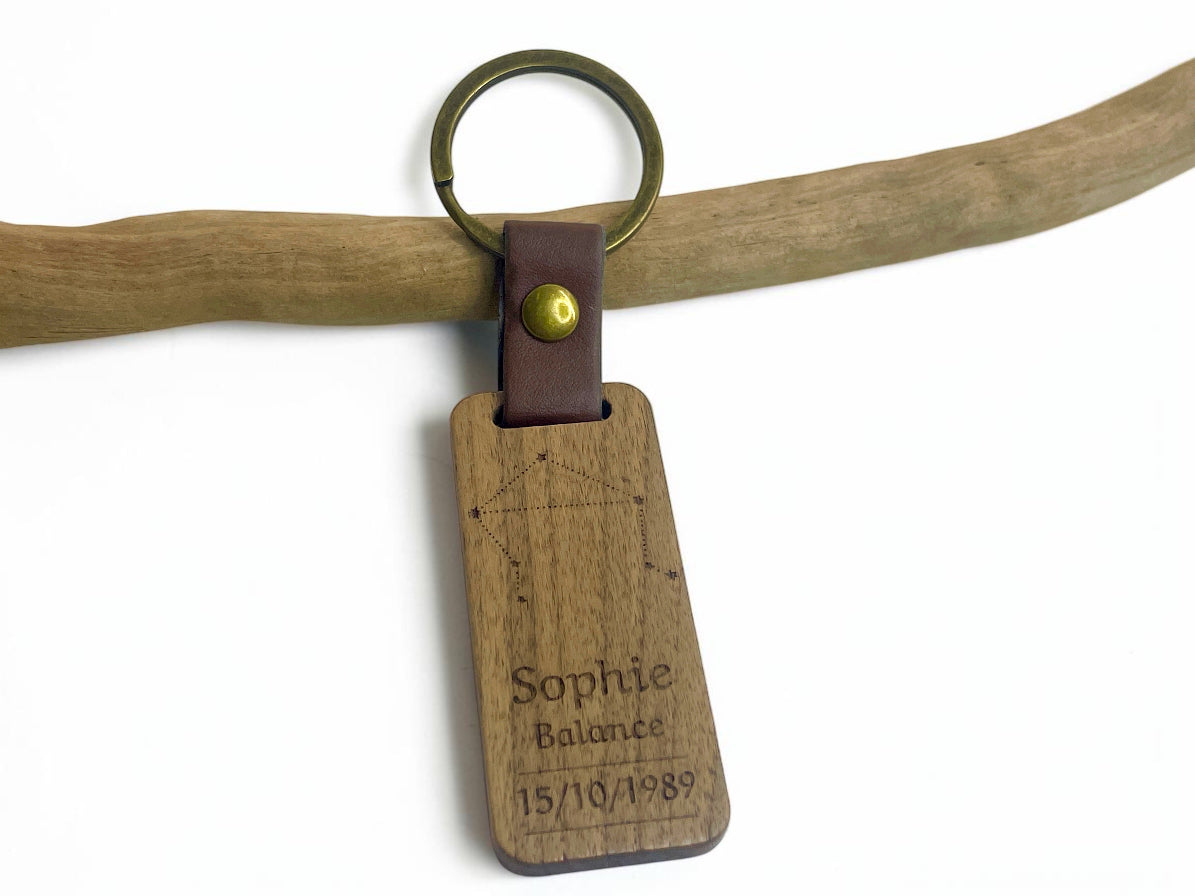 Porte-clés bois gravé prénom, signe astrologique et date de naissance, posé sur une branche
