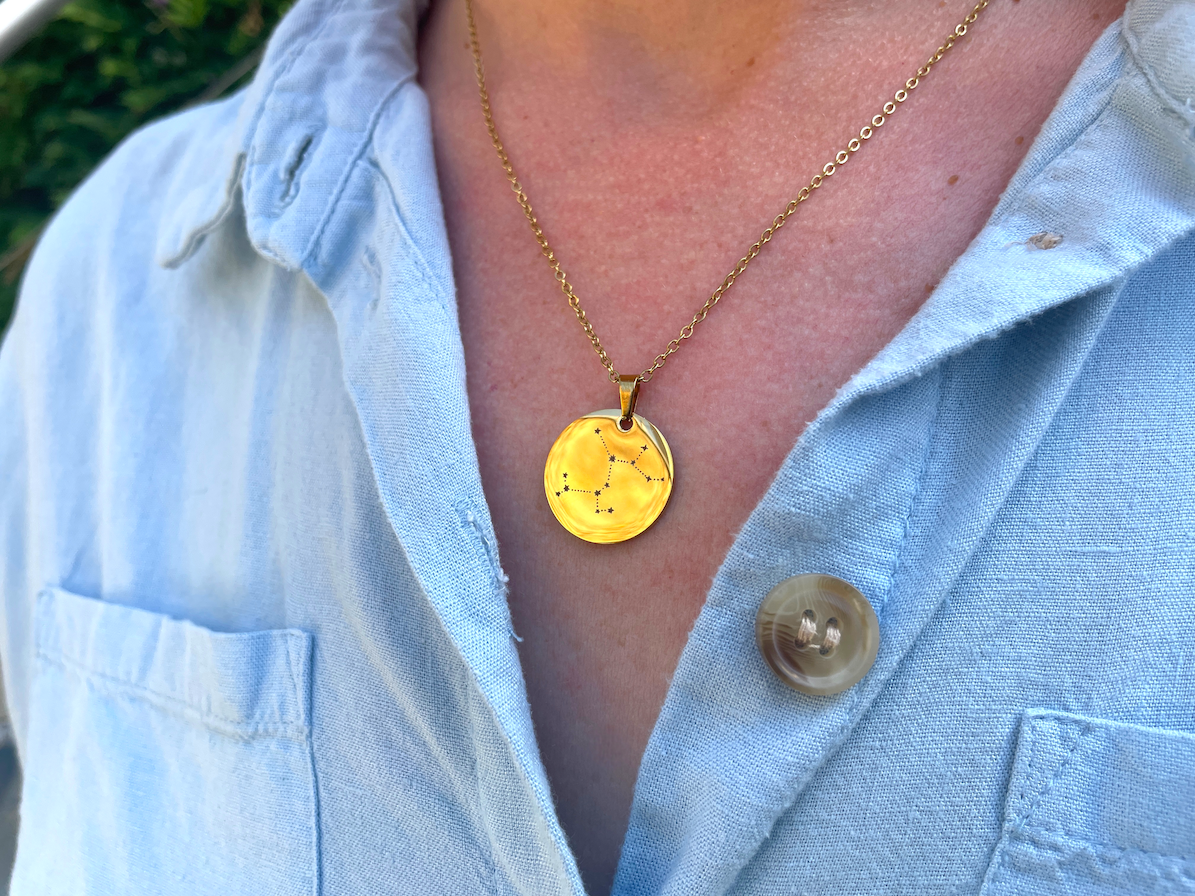Collier médaille dorée constellation Sagittaire porté au cou, sur une chemise bleu clair