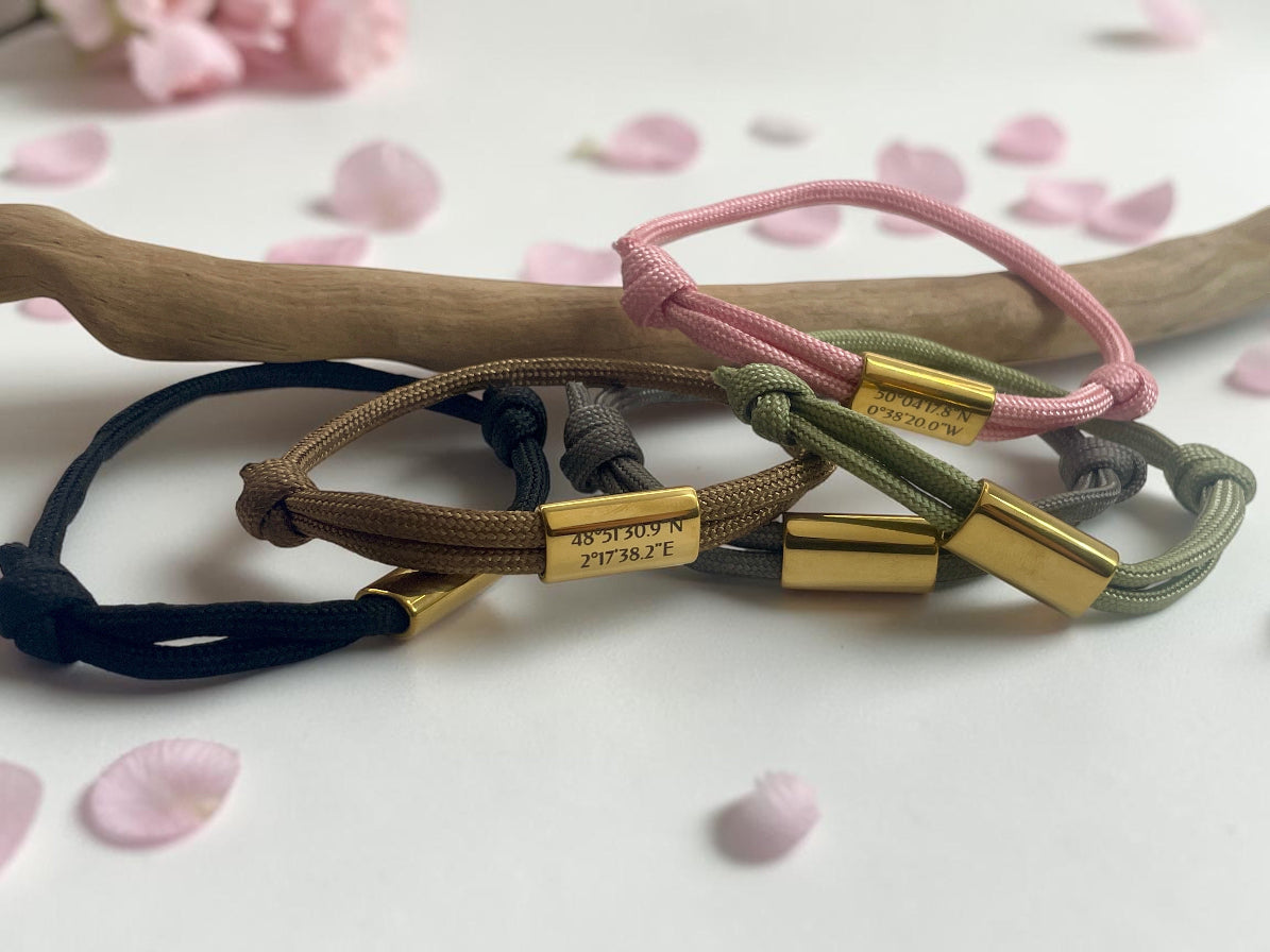 Plusieurs bracelets cordon à plaque dorée dans différents coloris, posés sur une branche