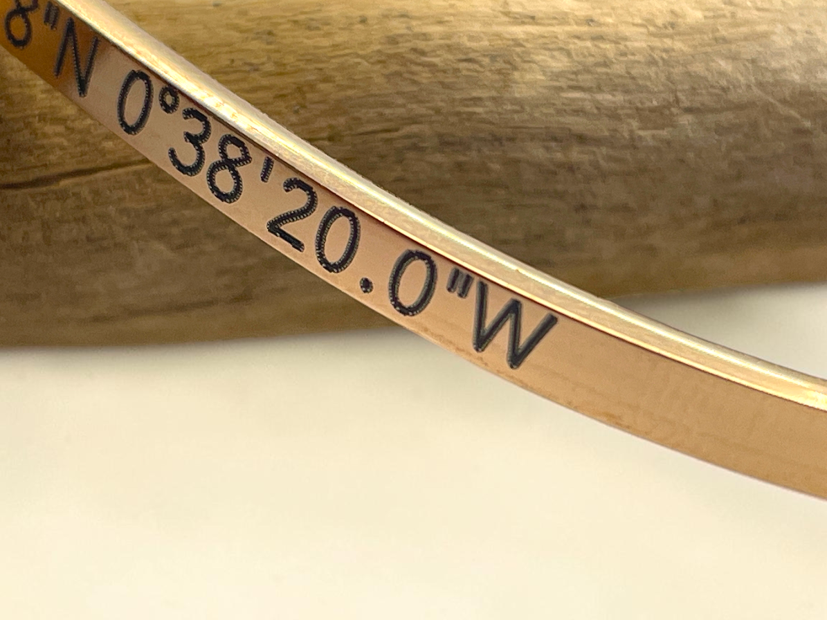 Gros plan de la gravure des coordonnées GPS en degrés, minutes et secondes sur bracelet doré