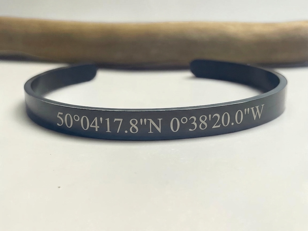 Bracelet jonc ouvert en acier noir gravé de coordonnées GPS, vue de trois quarts
