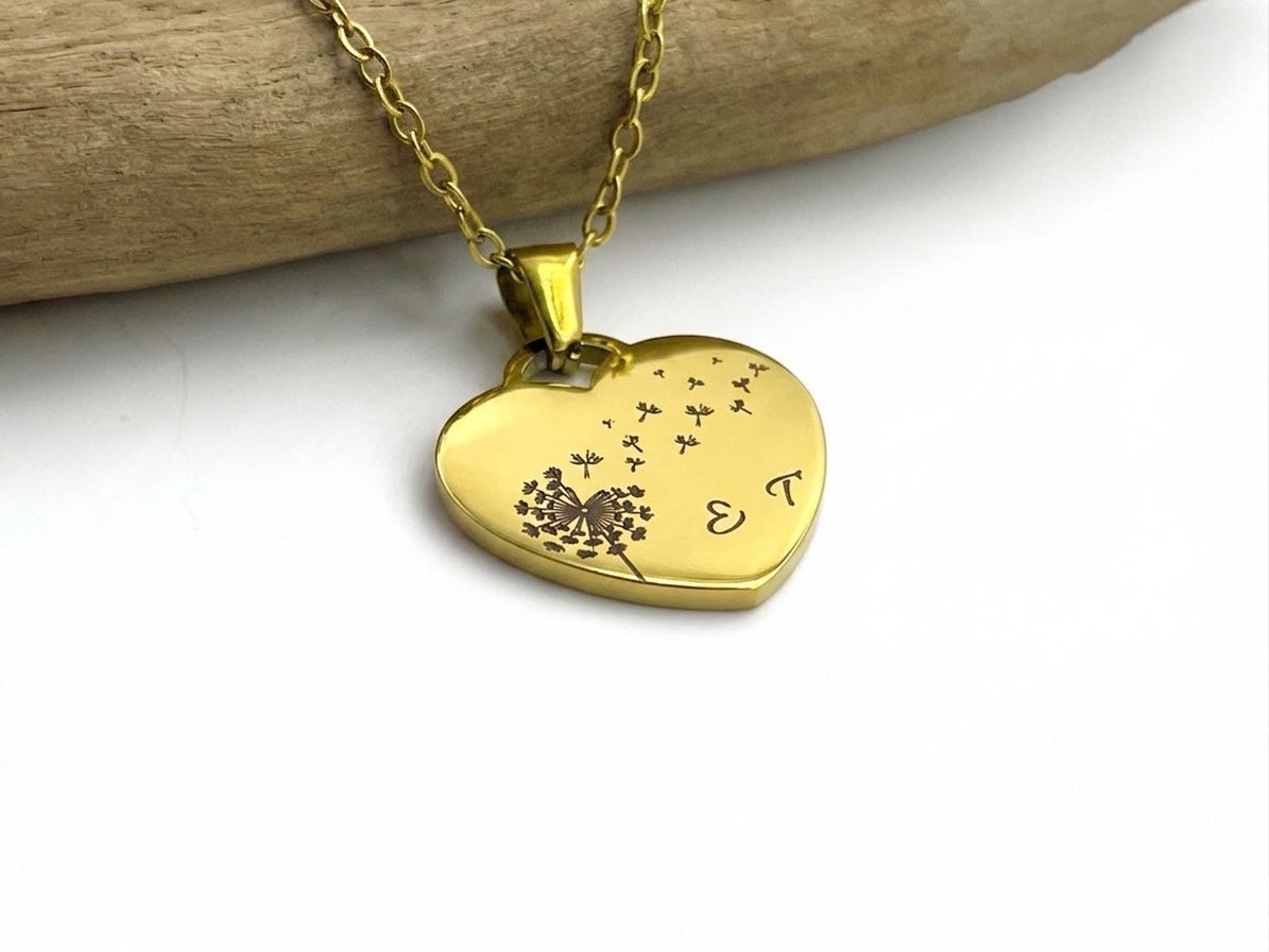 Collier cœur doré gravé d'un pissenlit sur sa chaîne fine, suspendu à une branche