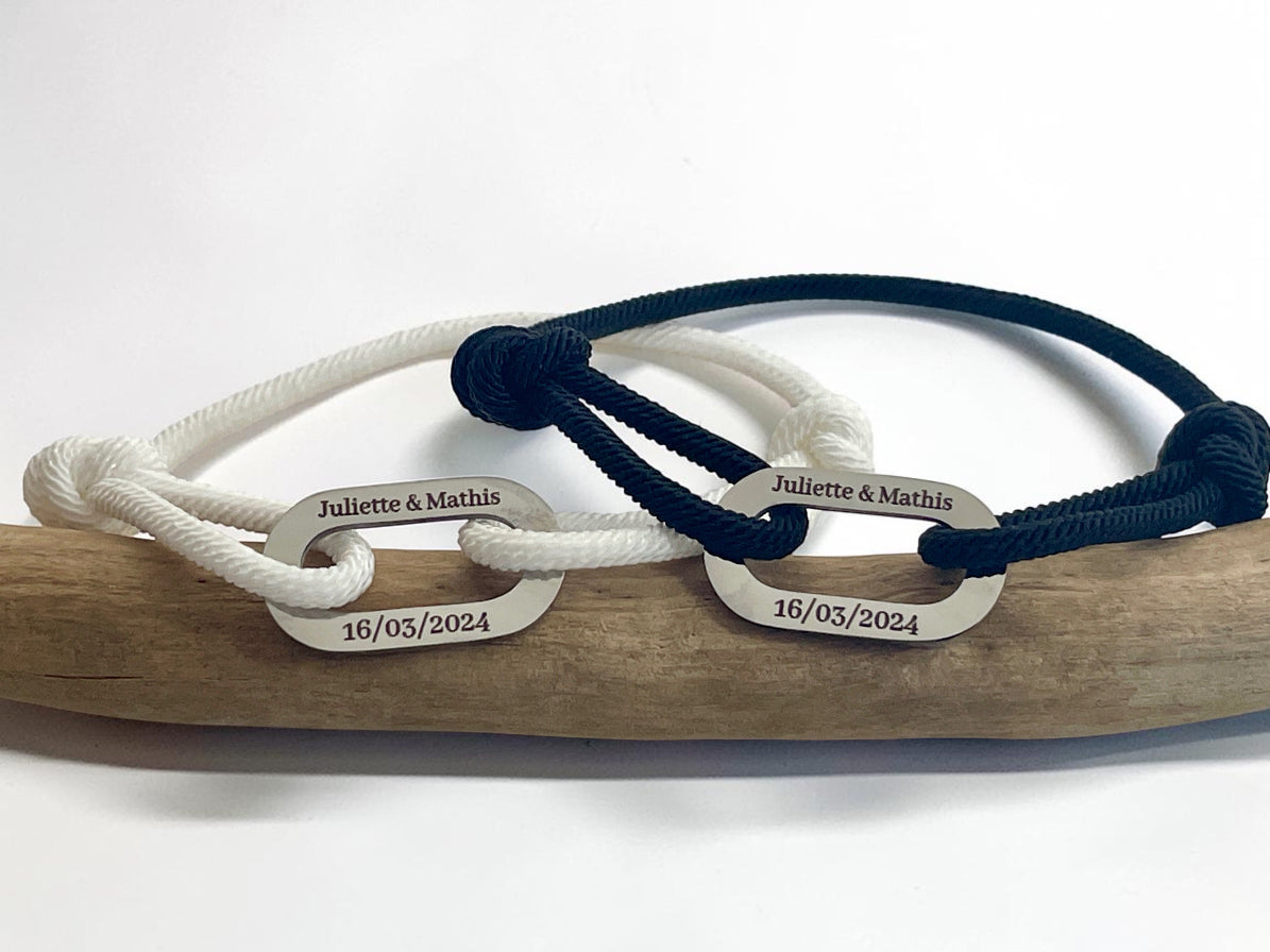 Deux bracelets cordon assortis gravés prénoms et date, posés sur une branche de bois