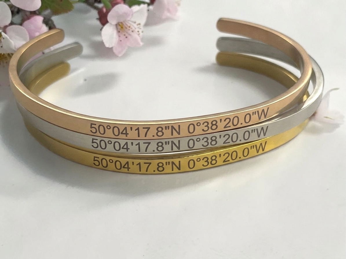 Trois bracelets joncs gravés de coordonnées GPS superposés, finitions dorée et argentée