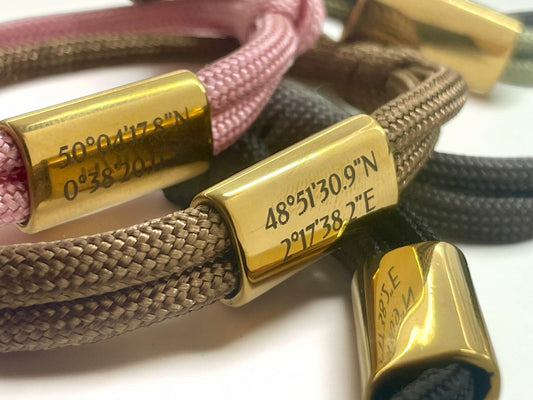 Gros plan de la gravure de coordonnées GPS sur les plaques dorées de deux bracelets
