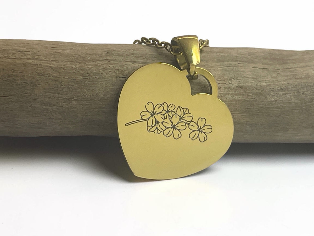 Collier cœur doré gravé d'une fleur à plusieurs corolles, suspendu à une branche