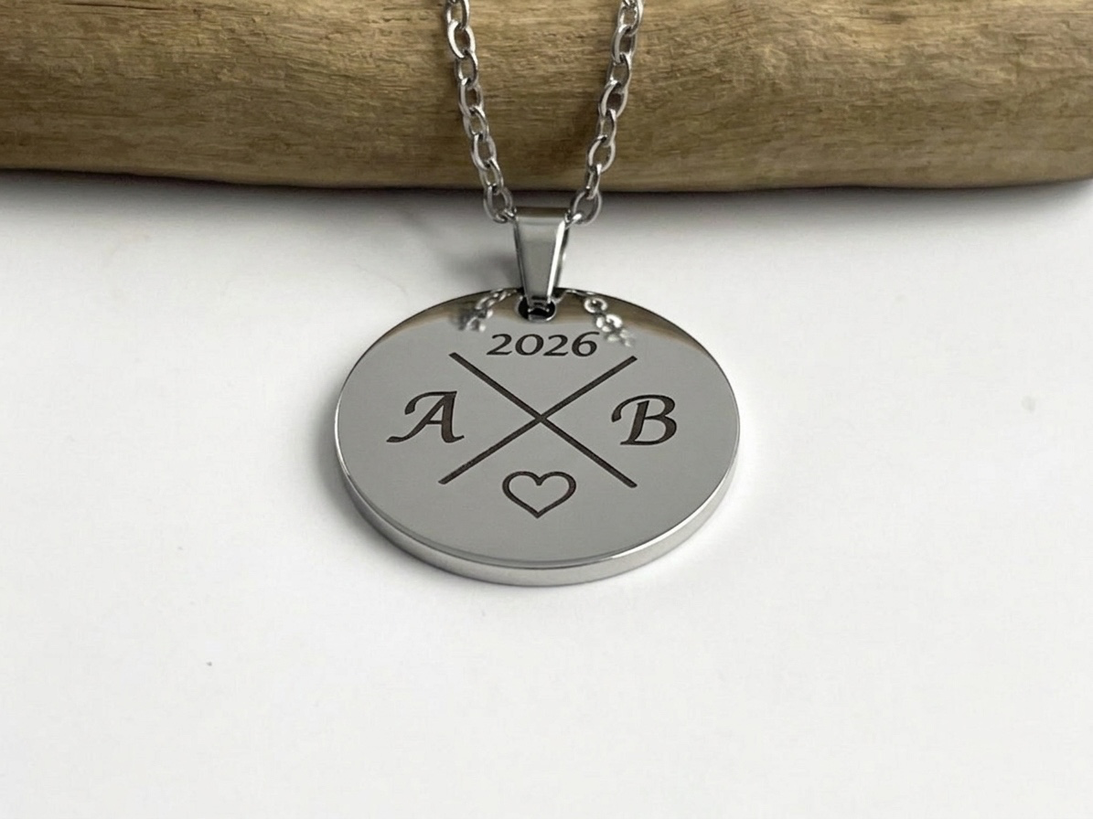 Collier médaille ronde argentée gravé des initiales et de l'année, posé sur une branche