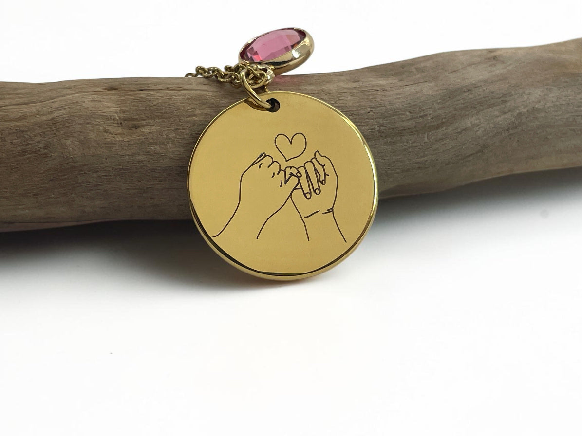 Collier médaille dorée gravée de mains formant un cœur, avec pierre de naissance rose