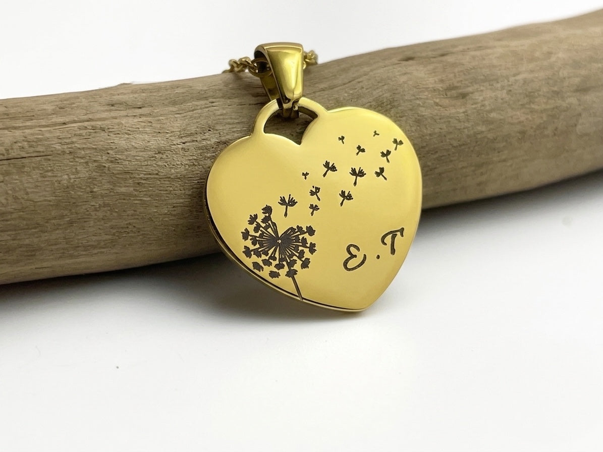 Collier cœur doré gravé d'un pissenlit et des initiales E et T, posé sur une branche de bois