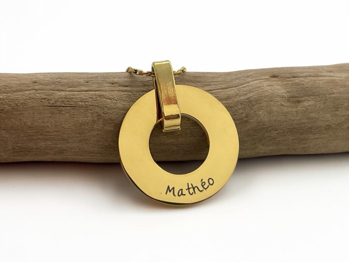 Collier médaille ajourée dorée gravée du prénom Mathéo, posé sur une branche de bois
