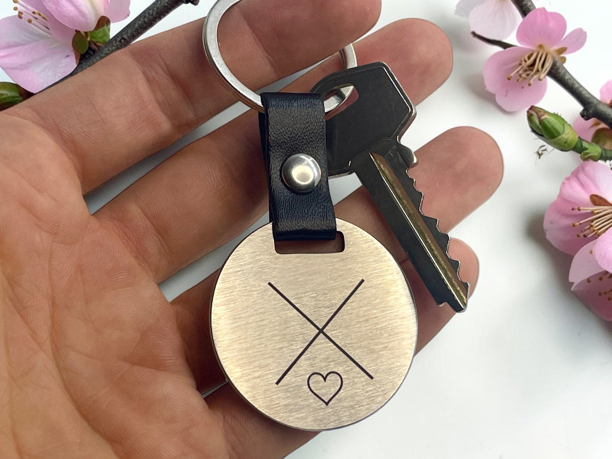 Porte-clés rond en acier gravé de deux initiales et d'un cœur, tenu en main avec une clé