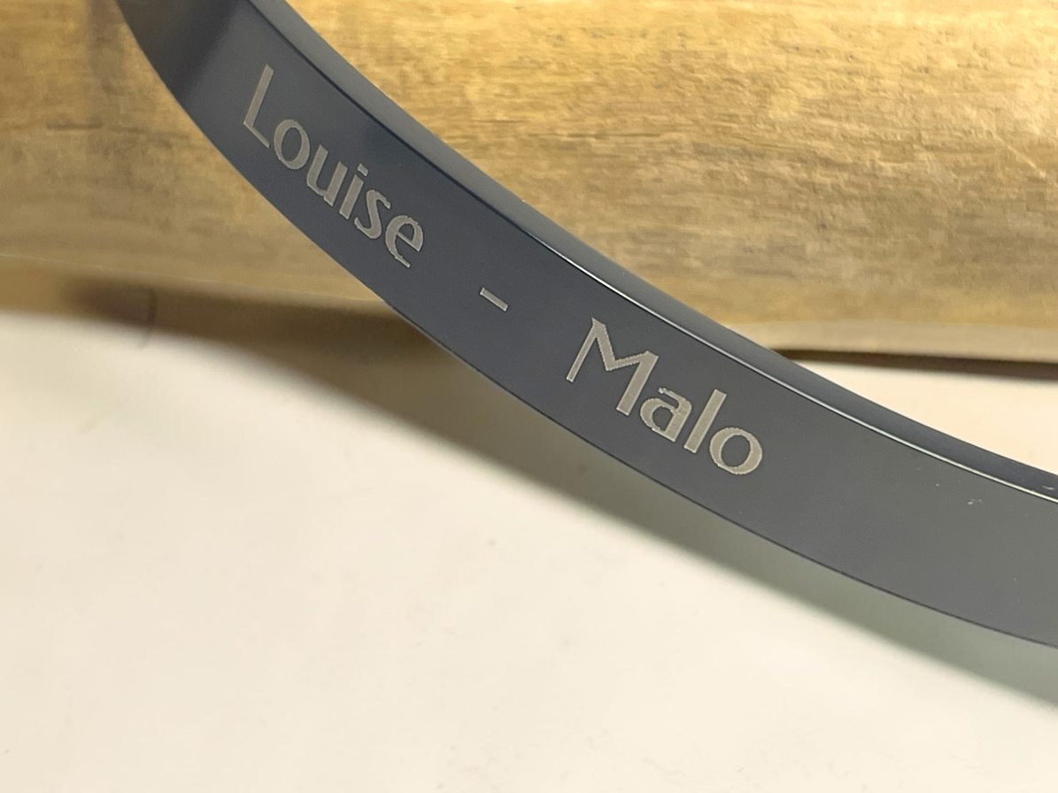 Gros plan de la gravure des prénoms Louise et Malo sur un bracelet jonc en acier noir