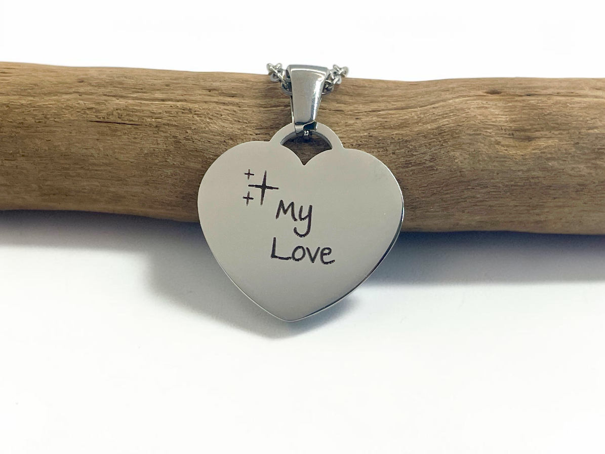 Collier cœur argenté gravé My Love, posé sur une branche de bois clair