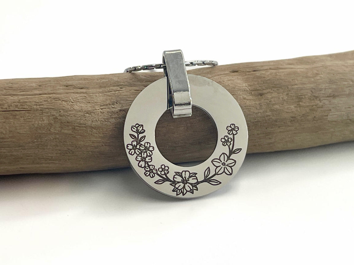 Collier médaille ajourée argentée gravée de fleurs, posé sur une branche de bois