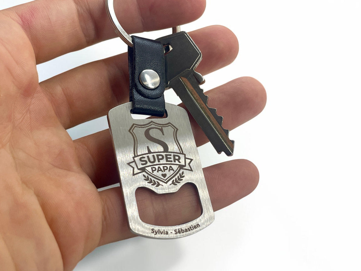 Porte-clés décapsuleur Super Papa tenu en main avec des clés, pour montrer sa taille réelle