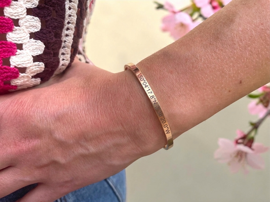 Bracelet jonc or rose coordonnées GPS porté au poignet, décor de fleurs de cerisier