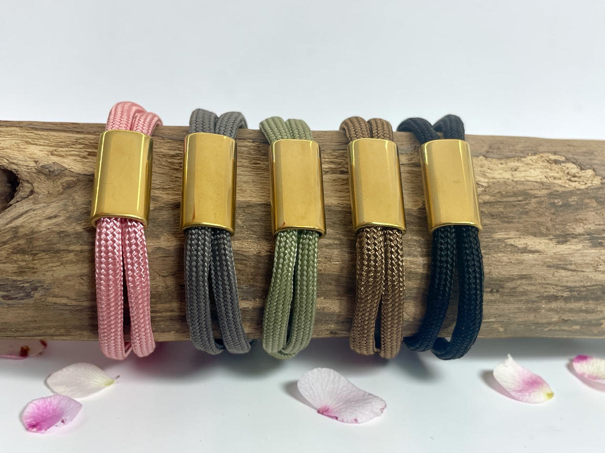 Cinq bracelets cordon à plaque dorée alignés sur une branche, nuancier des coloris disponibles