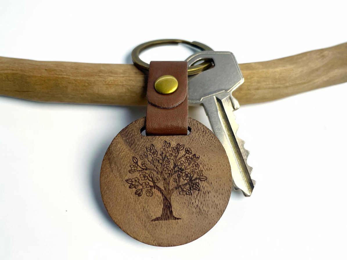 Porte-clés bois rond gravé d'un arbre de vie, lanière cuir marron, suspendu à une branche avec une clé