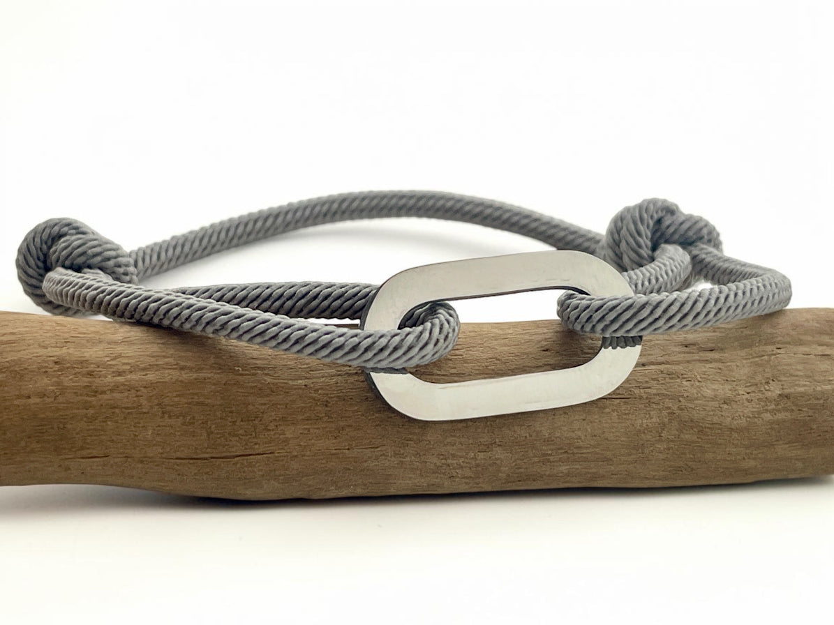 Bracelet cordon gris ajustable avec maillon acier à graver, posé sur une branche de bois