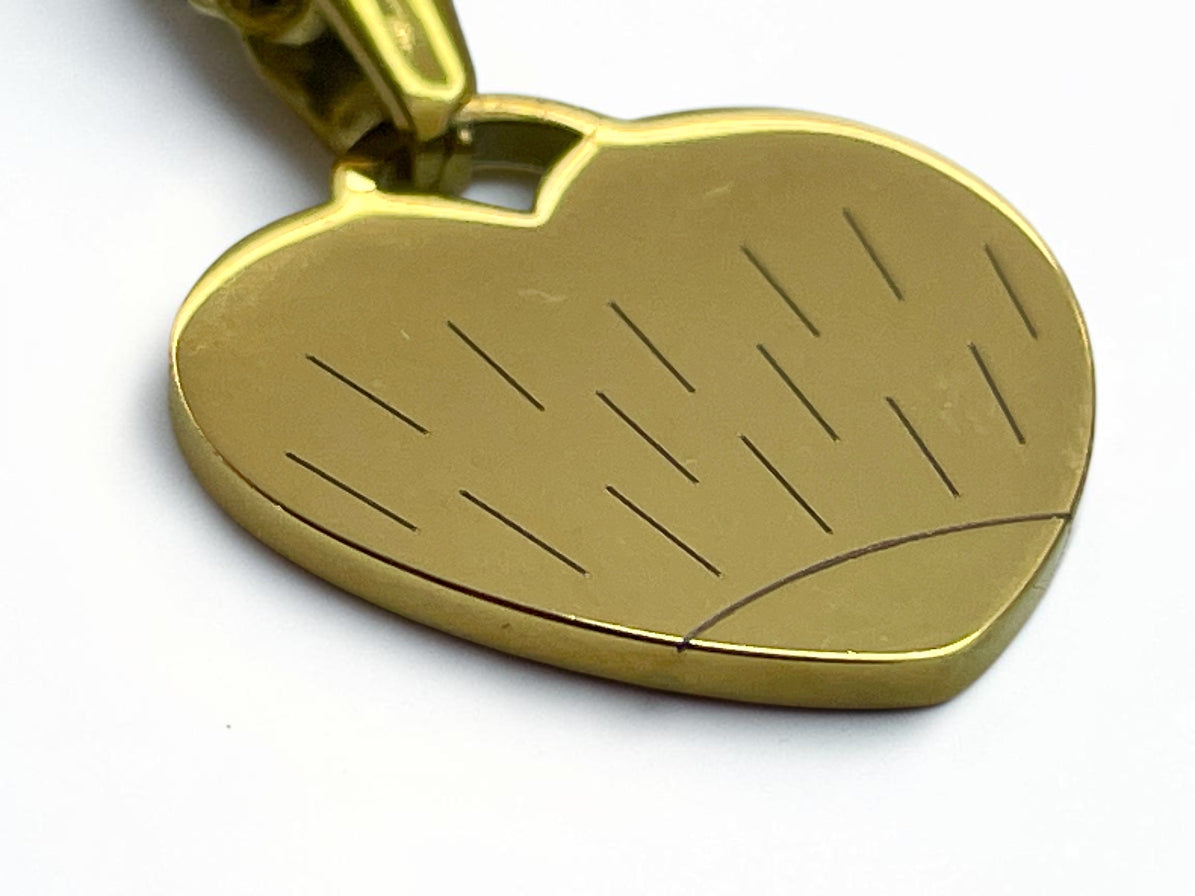 Gros plan du motif soleil gravé sur un collier cœur en acier doré