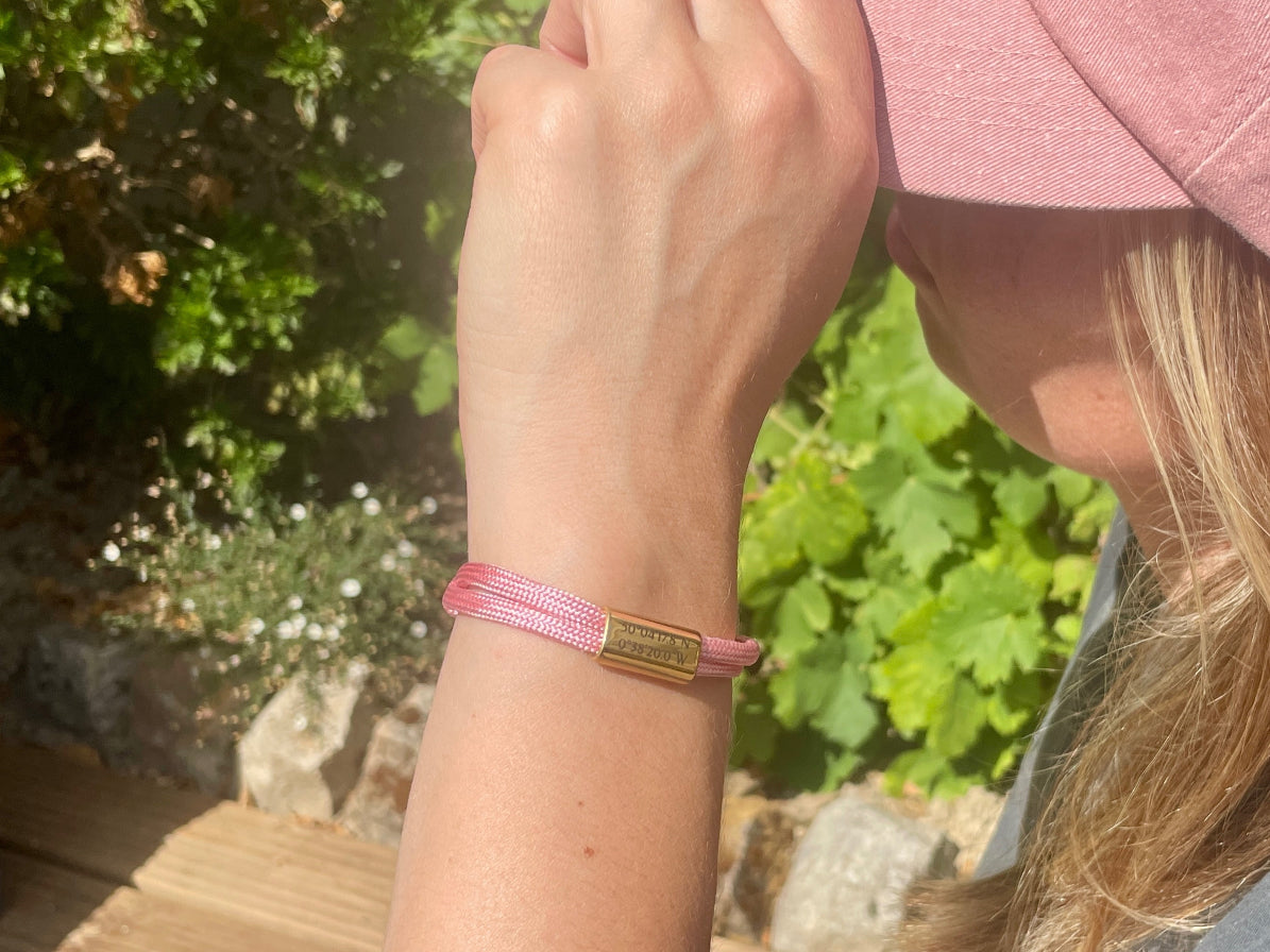Bracelet cordon rose à plaque dorée porté au poignet, en extérieur