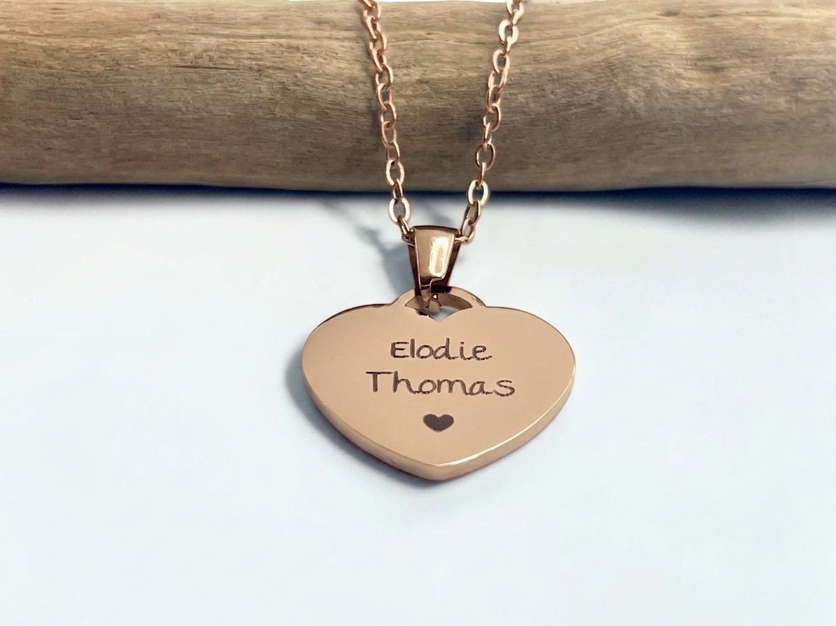 Collier cœur or rose gravé de deux prénoms avec un cœur, suspendu à une branche
