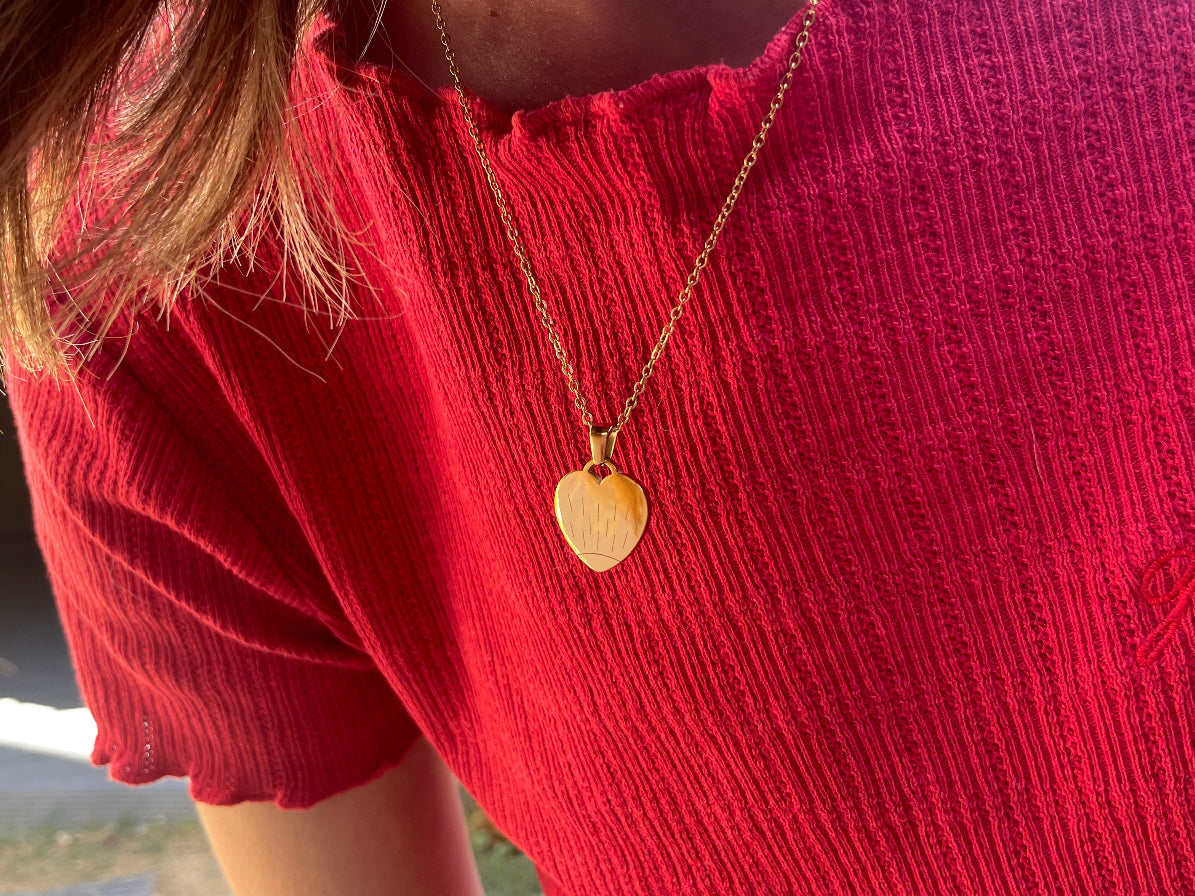 Collier cœur doré gravé d'un soleil porté au cou, sur un haut rouge