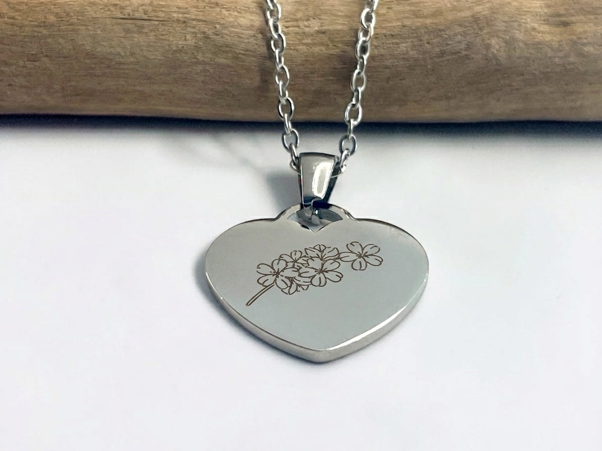 Collier cœur en acier argenté gravé d'une fleur, porté sur sa chaîne fine