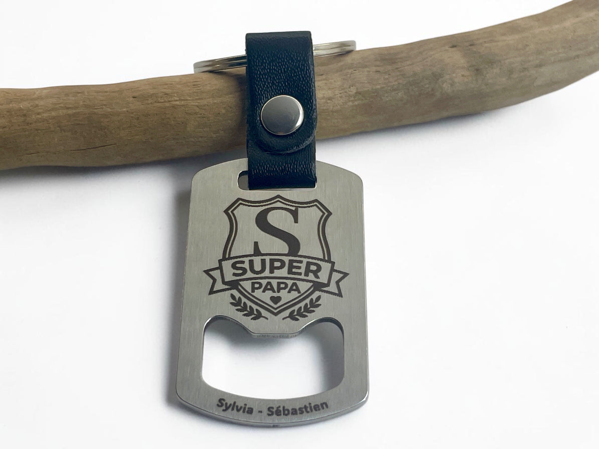 Porte-clés décapsuleur gravé Super Papa posé sur une branche, prénoms gravés au bas
