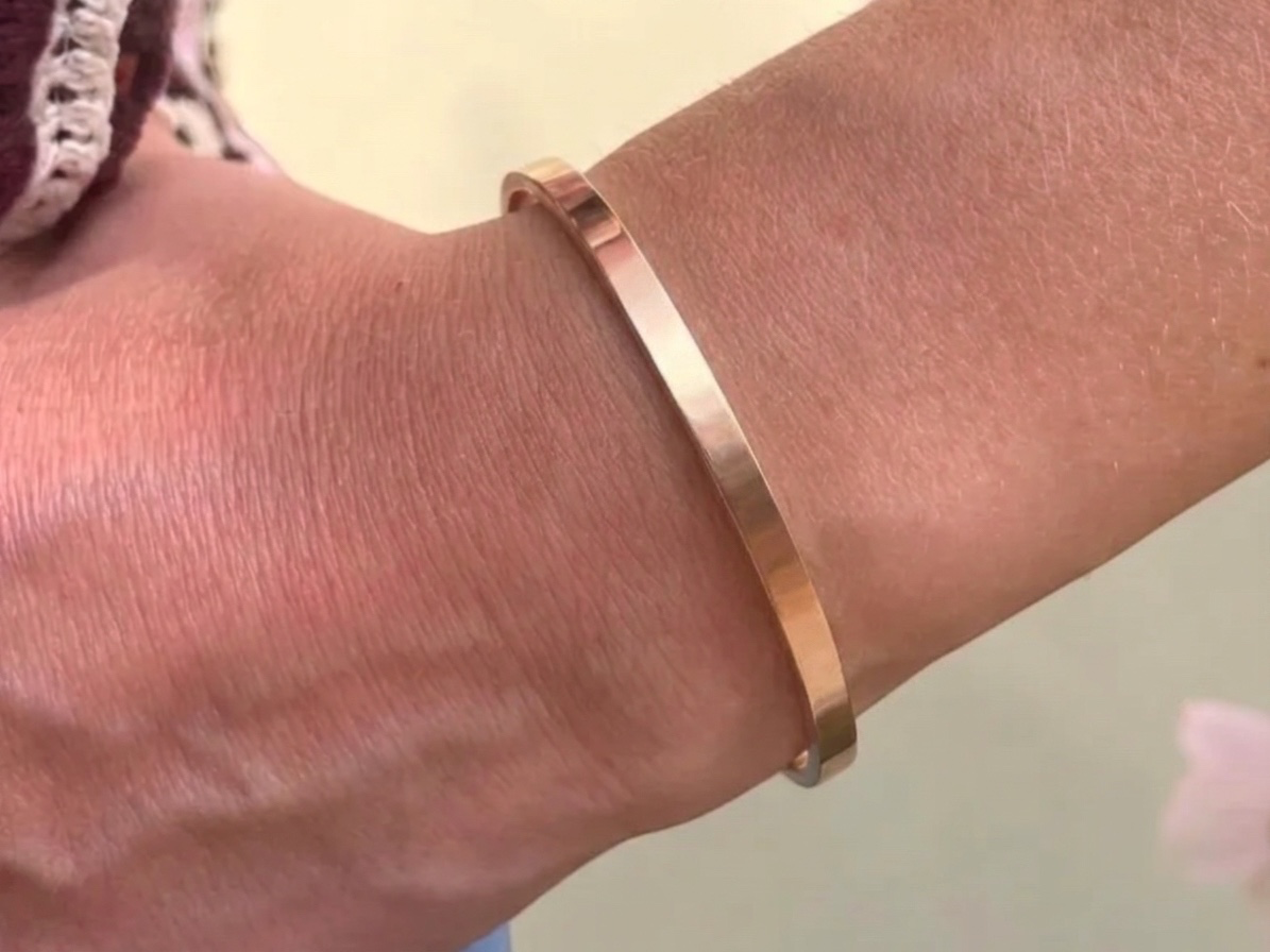 Bracelet jonc ouvert or rose porté au poignet, gravure fine coordonnées GPS