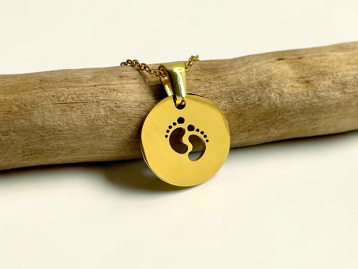 Collier médaille dorée ajourée gravée de deux petits pieds de bébé, suspendu à une branche