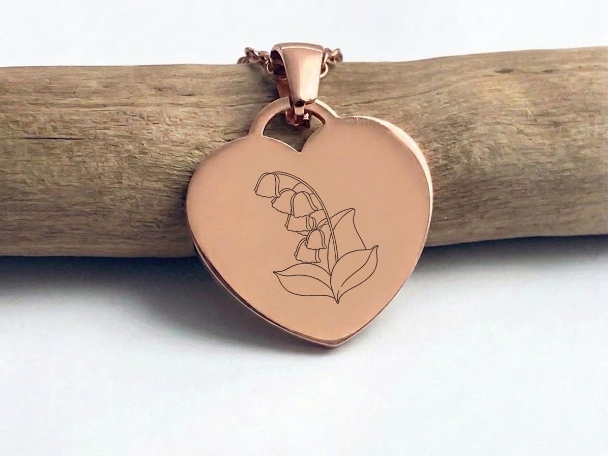 Collier cœur or rose gravé d'une fleur au trait fin, suspendu à une branche