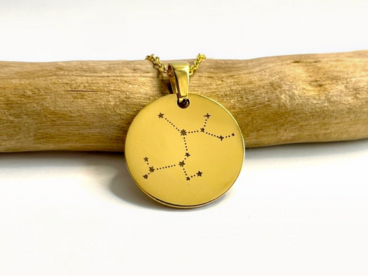 Collier médaille dorée gravée de la constellation du Sagittaire, posé sur une branche de bois