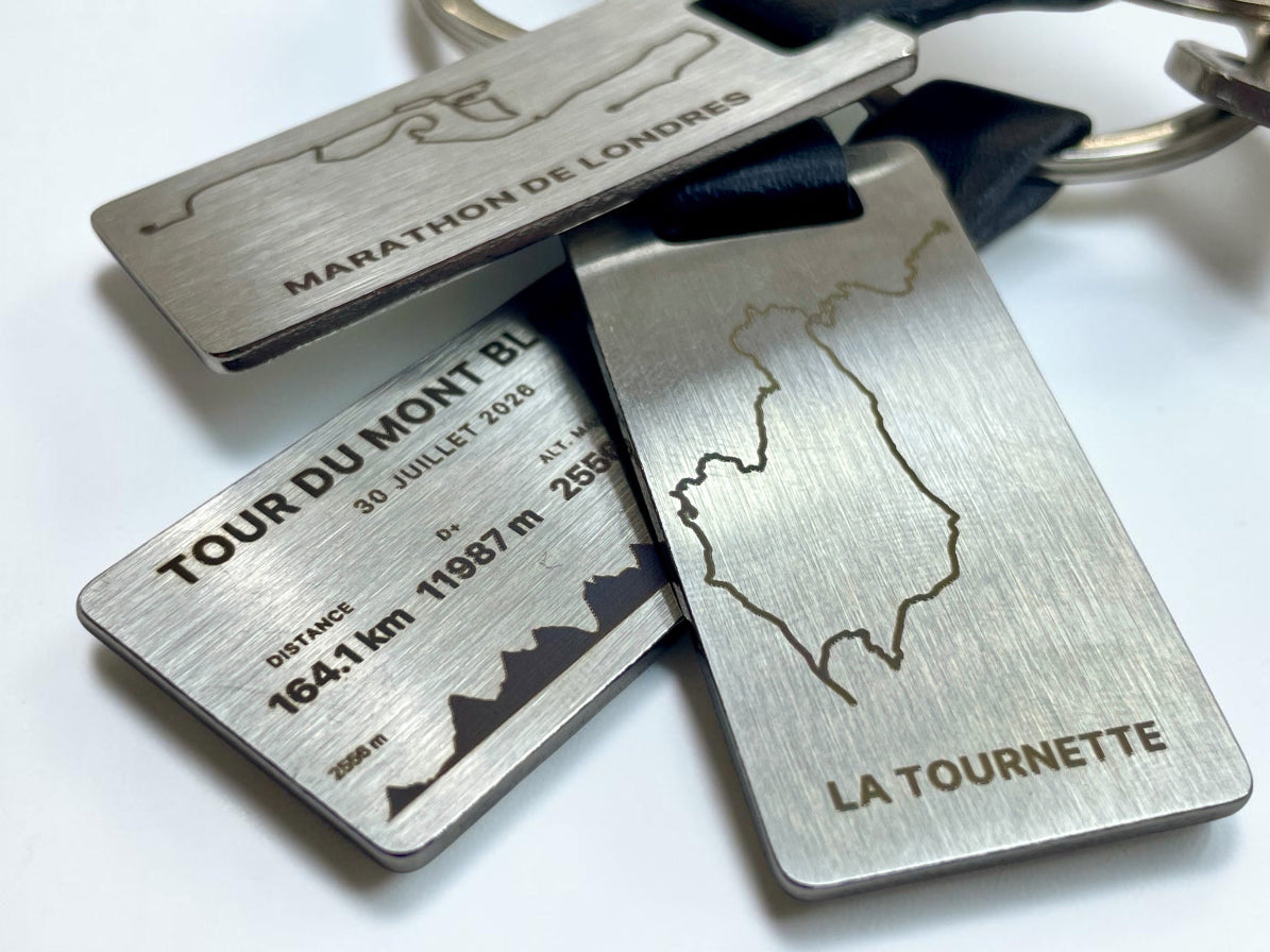 Trois porte-clés GPX en acier gravés de tracés de randonnée et de course superposés