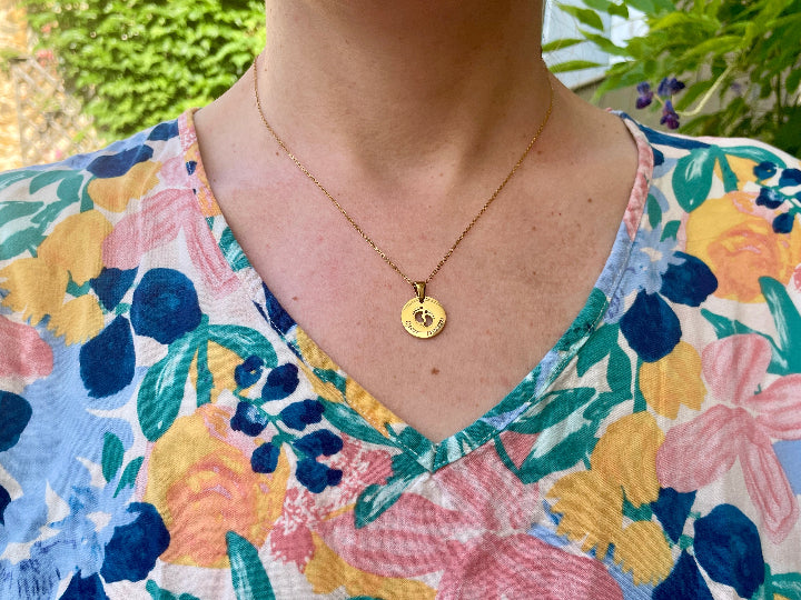 Collier médaille pieds de bébé porté au cou, sur un haut fleuri
