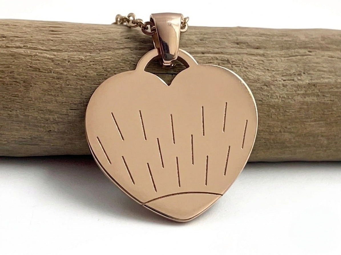 Collier cœur or rose gravé d'un motif soleil, suspendu à une branche de bois