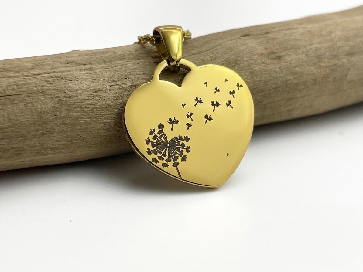 Collier cœur doré gravé d'un pissenlit dont les akènes s'envolent, suspendu à une branche