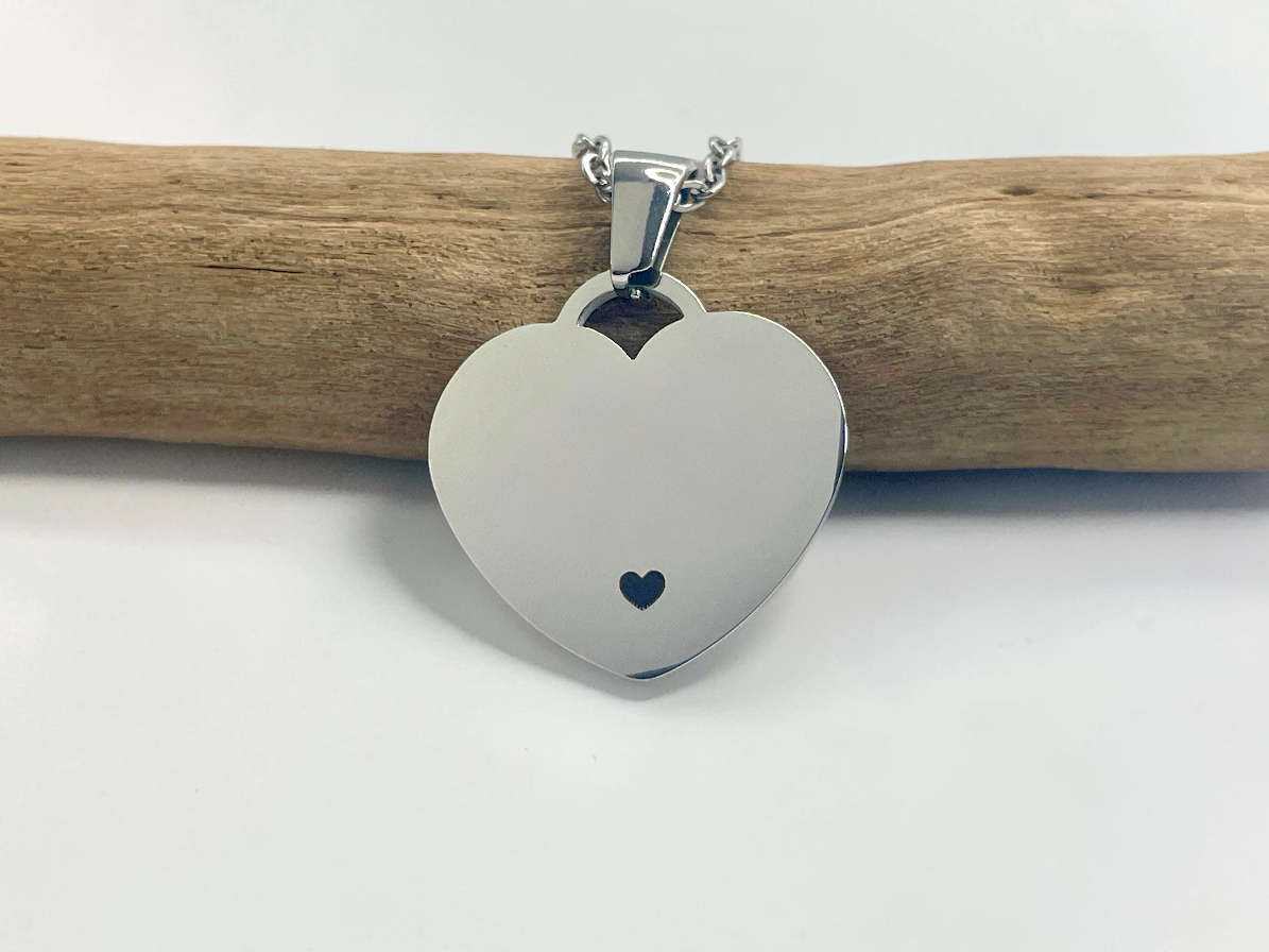 Collier cœur en acier argenté avec petit cœur gravé, suspendu à une branche de bois