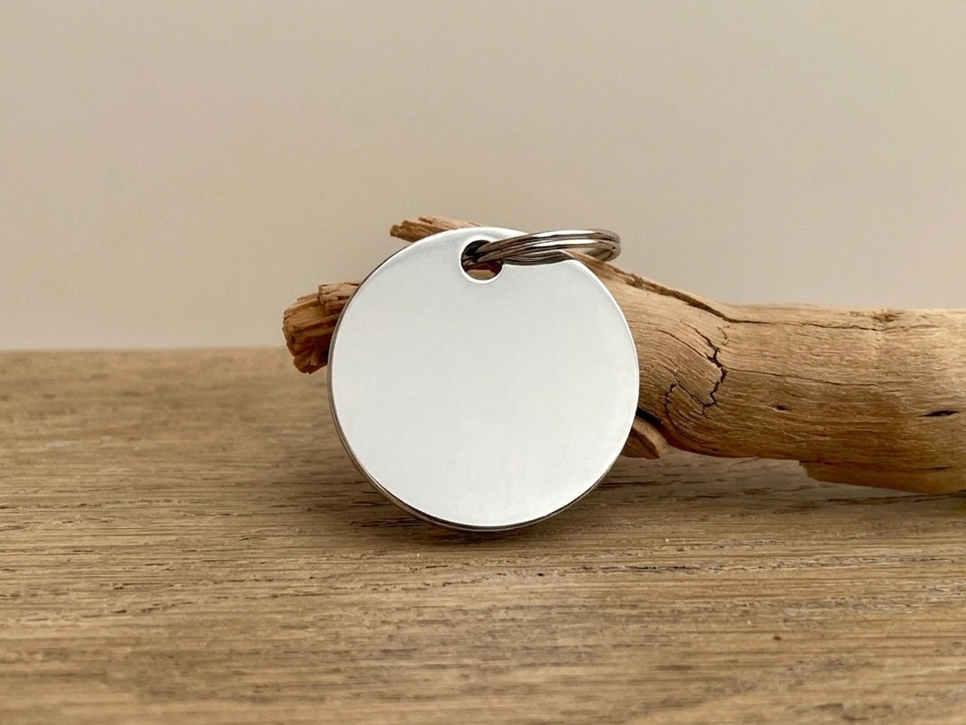 Médaille pour chien ronde en acier inoxydable Atelier Shironeko posée sur un morceau de bois flotté